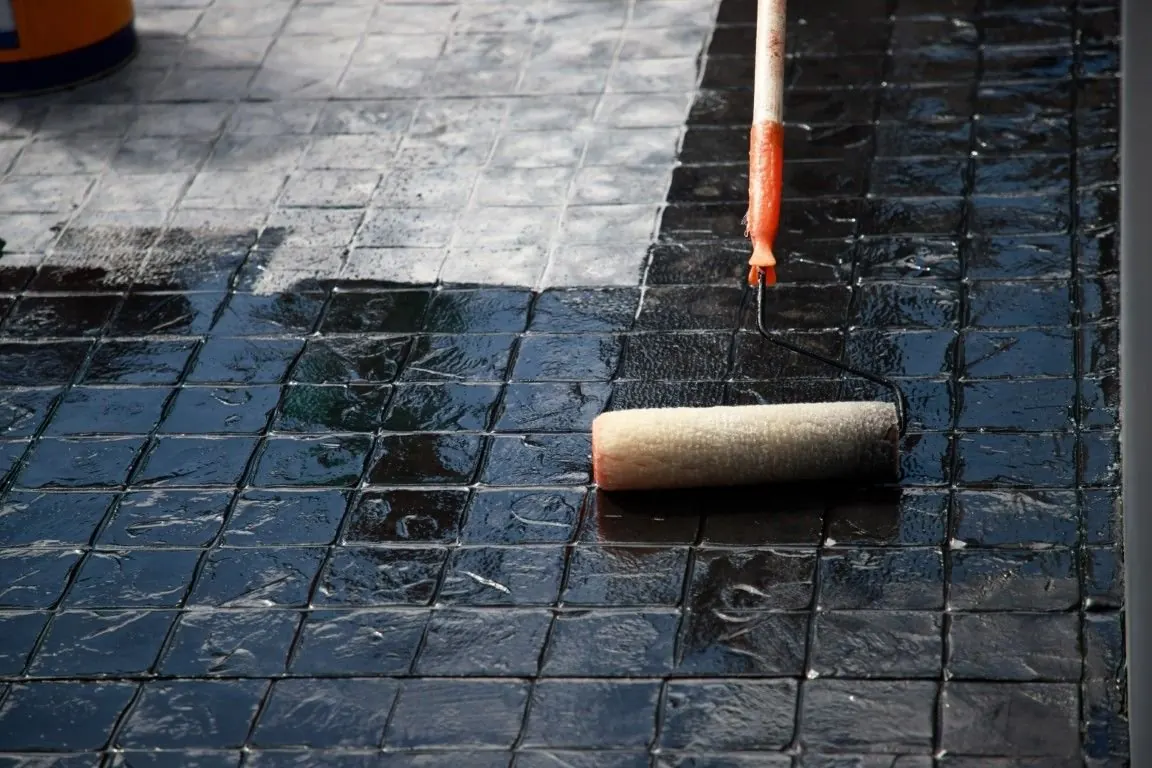 Roller applying clear sealer to dark stamped concrete at a home in Little Elm, TX